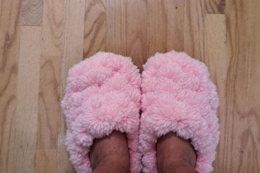 Pieds chaussés de pantoufles roses pelucheuses sur parquet